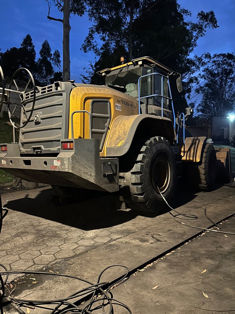 Pá carregadeira atendida à noite, com mangueira de ar ligada ao pneu